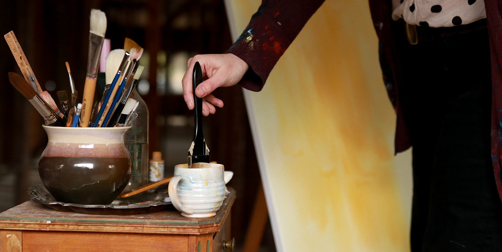 An artist reaching for a tool beside a pot of brushes in the lodge studio