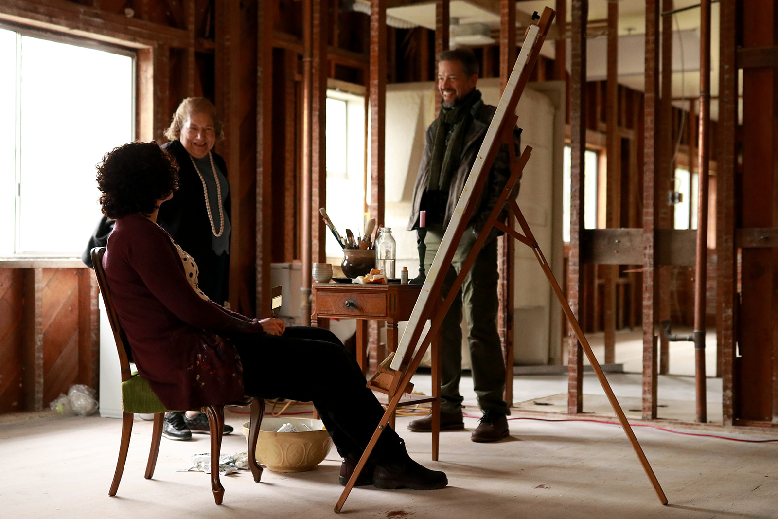 Three people laughing together around an easel in the historic lodge