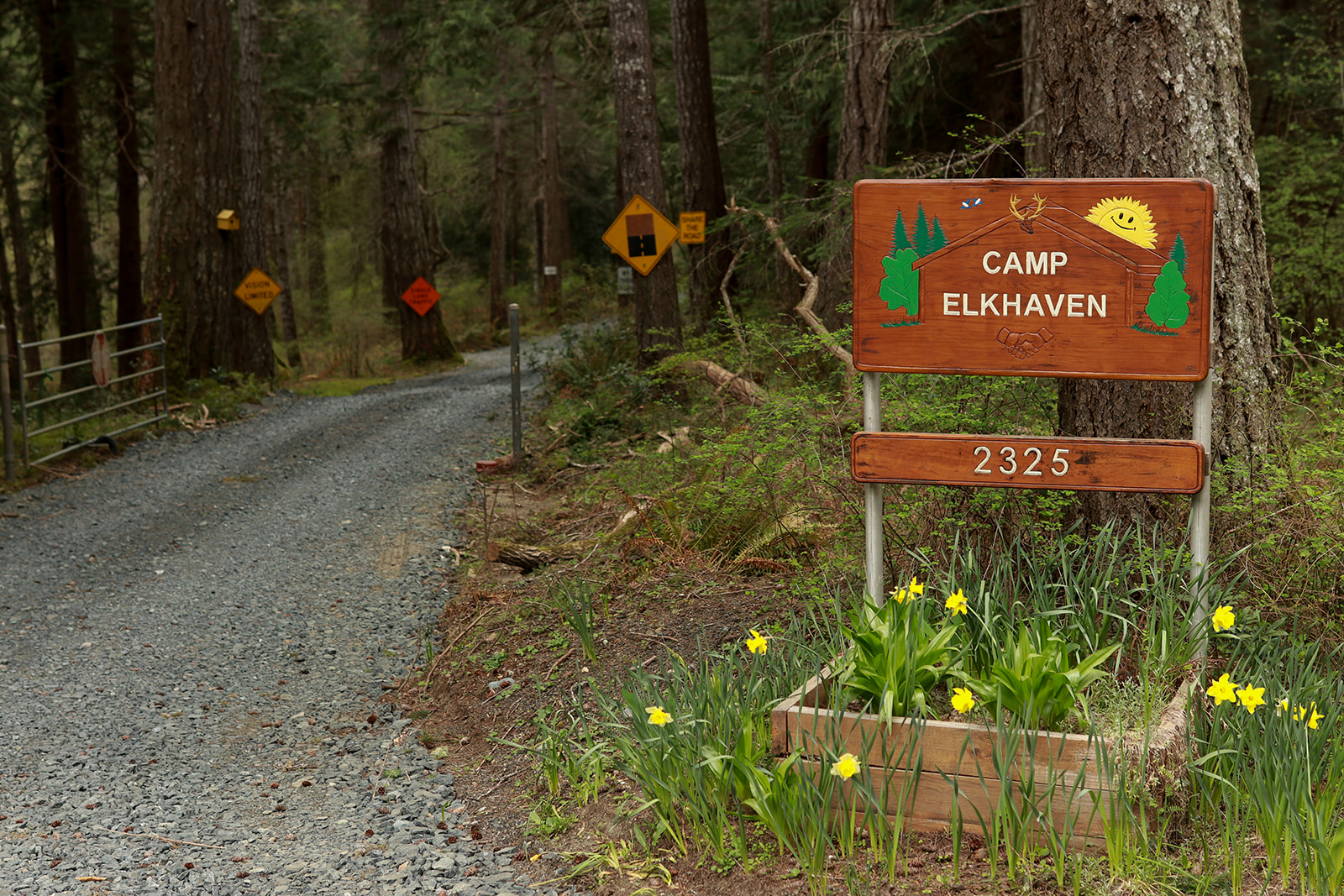 A wooden Camp Elkhaven sign beside the gravel drive into the forest