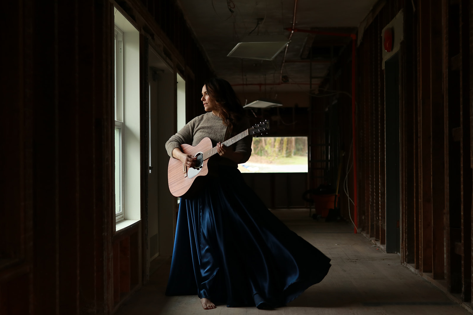 A musician playing guitar in the light of a window in the stripped-back lodge